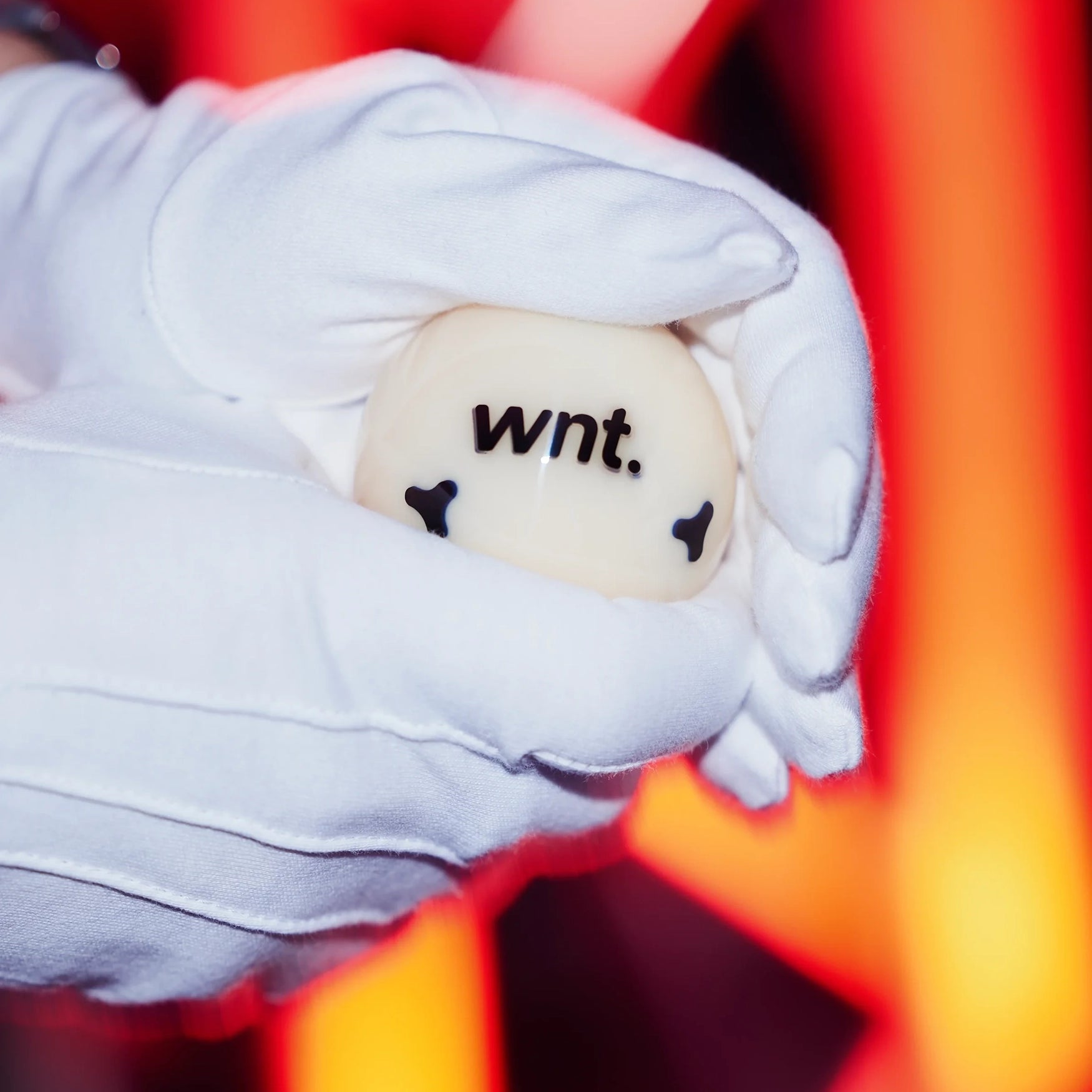 White gloves holding cue ball with 'wnt.' text against a blurred red and orange background